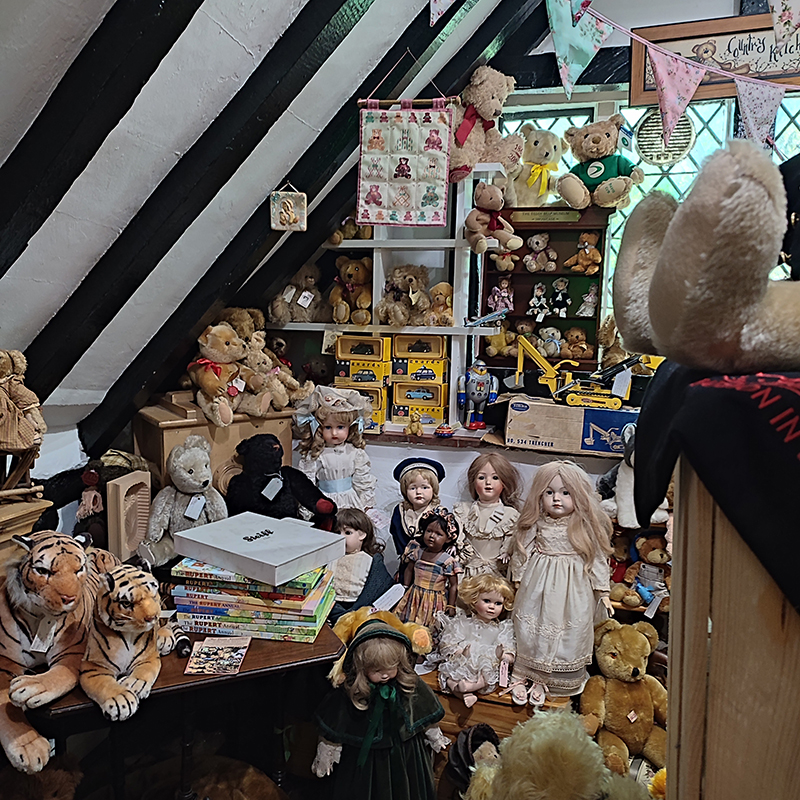 a room in an antique store with dolls and teddy bears on the shelves